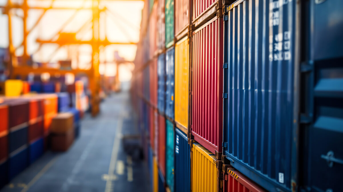 Stacks of colorful shipping containers at a port during sunset.