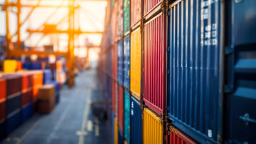 Stacks of colorful shipping containers at a port during sunset.