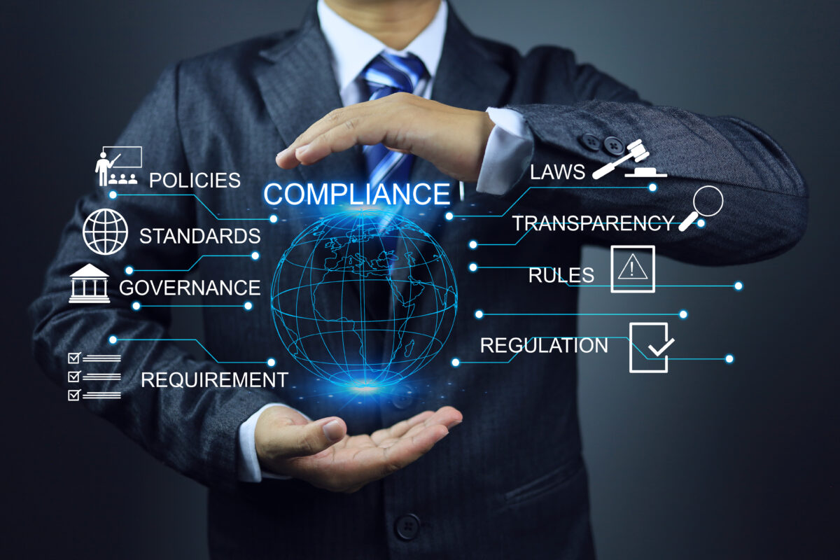 Businessperson holding a digital globe with compliance-related icons and terms.
