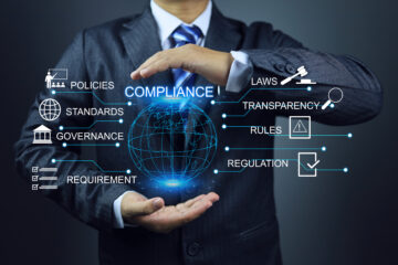 Businessperson holding a digital globe with compliance-related icons and terms.